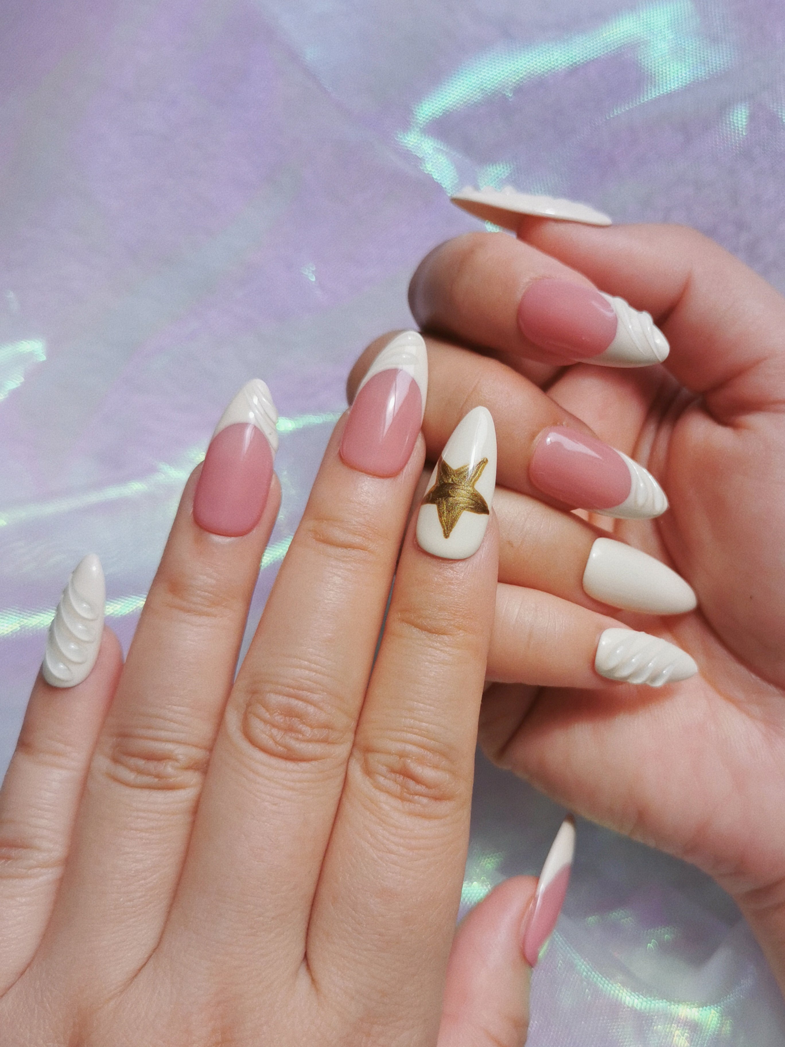 Milk white sculpted almond nails with blush base and gold star worn on both hands